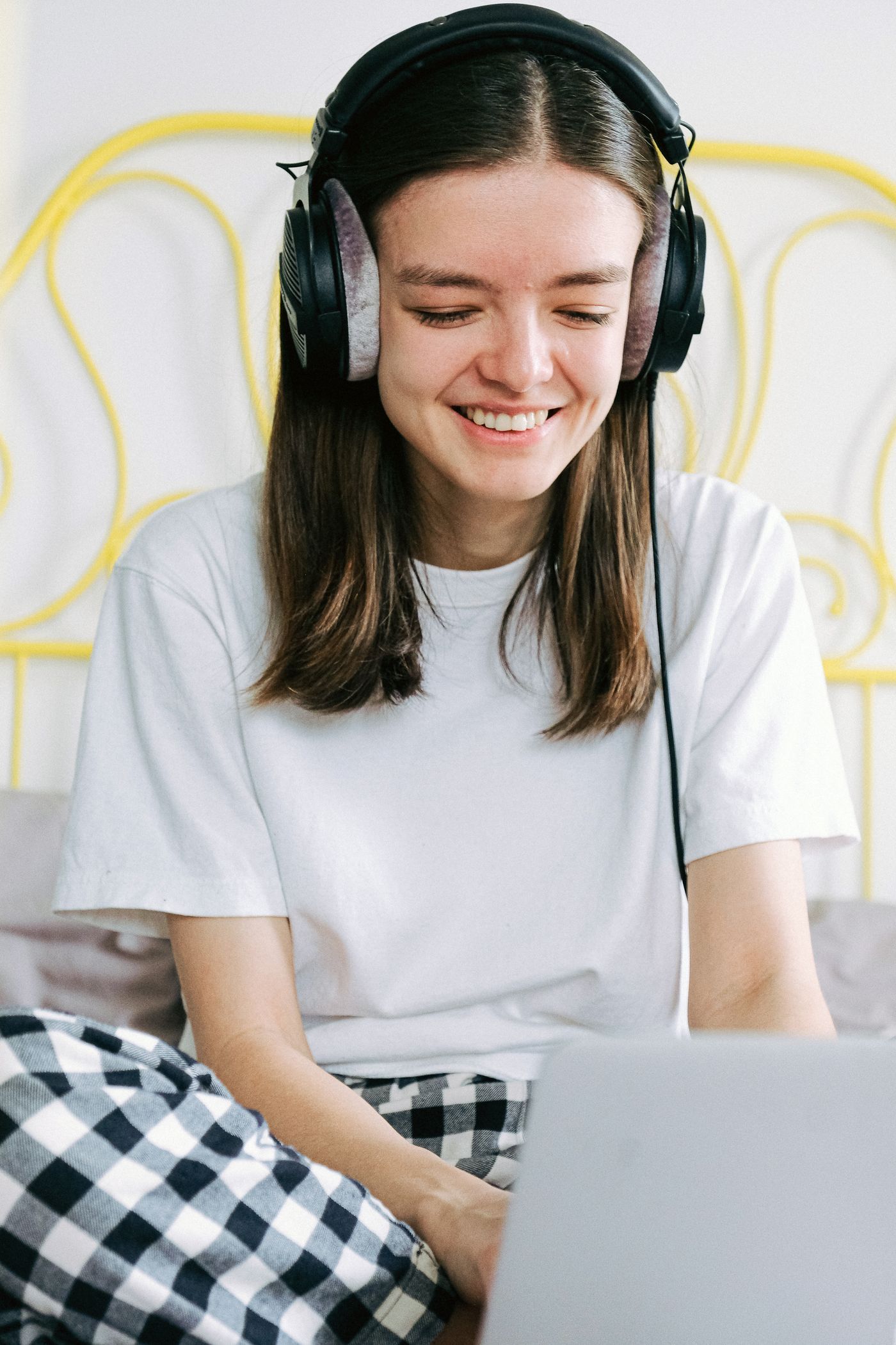 Studentka w słuchawkach uśmiecha się przy laptopie